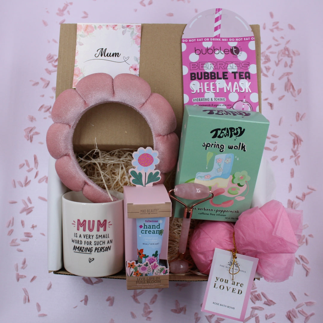 Gift set with various items including a pink headband, bubble tea sheet mask, and hand cream on a decorative background.