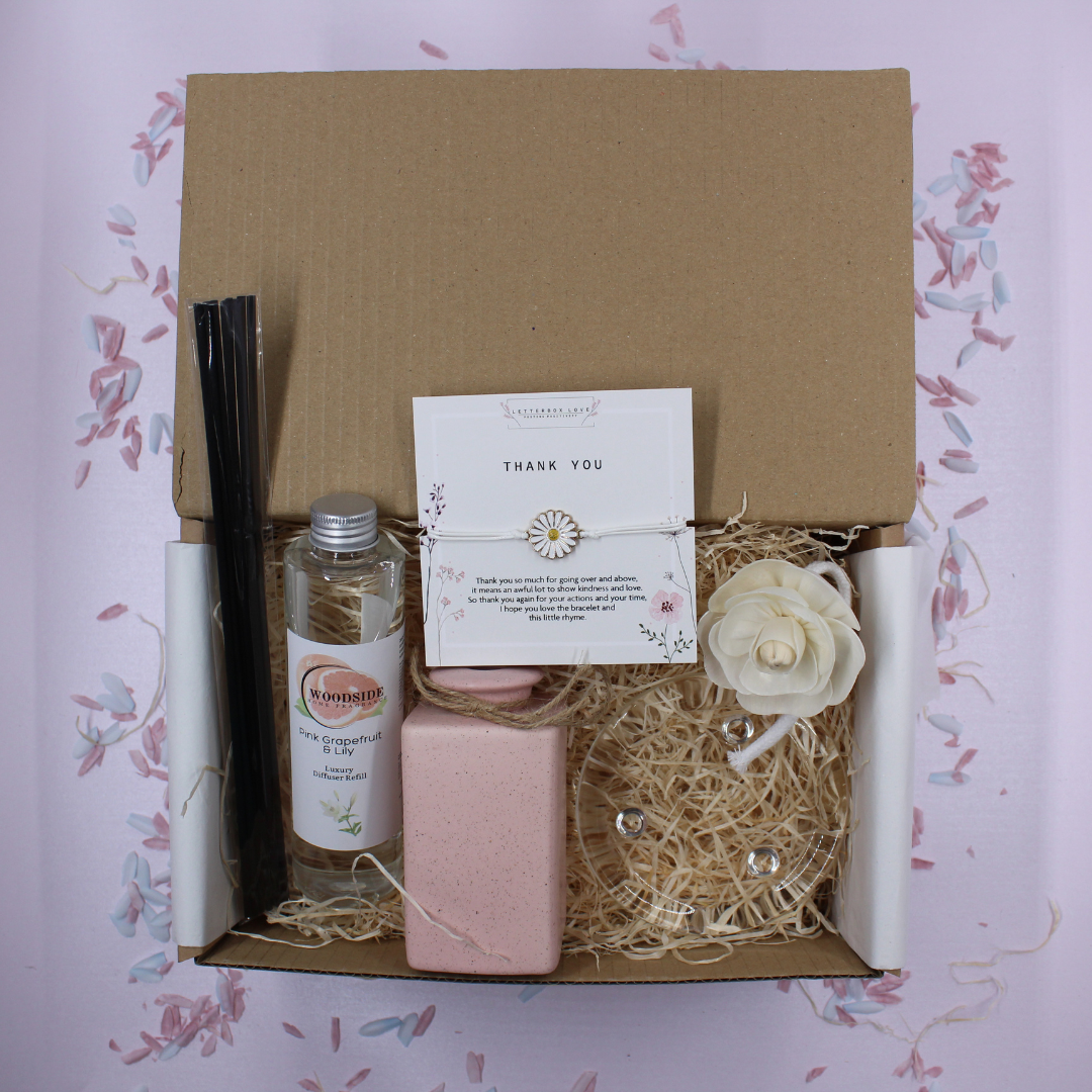 Gift box with stationery items including a card, pen, and small bottle on a floral-patterned background.