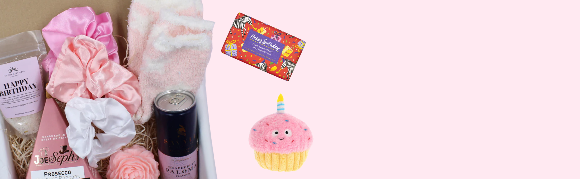 Gift set with bath bombs, flowers, and a candle on a pink background